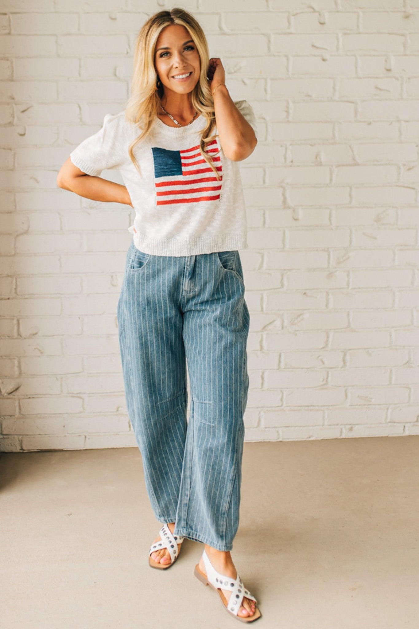 BLONDE WOMAN WEARING A WHITE AMERICAN FLAG TOP WITH SHIRRING DETAILS SHORT SLEEVES SWEATER TOP.