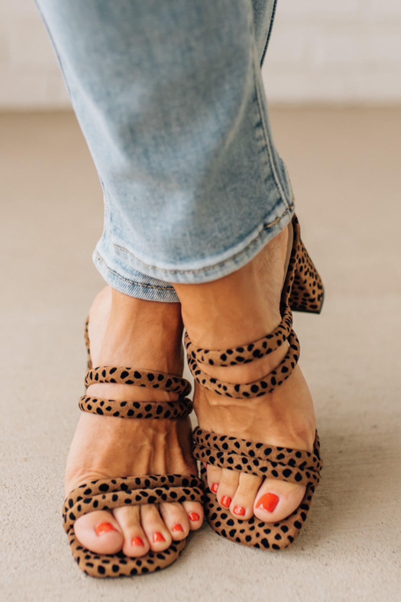 Leopard print sandals worn with light blue jeans on a neutral background