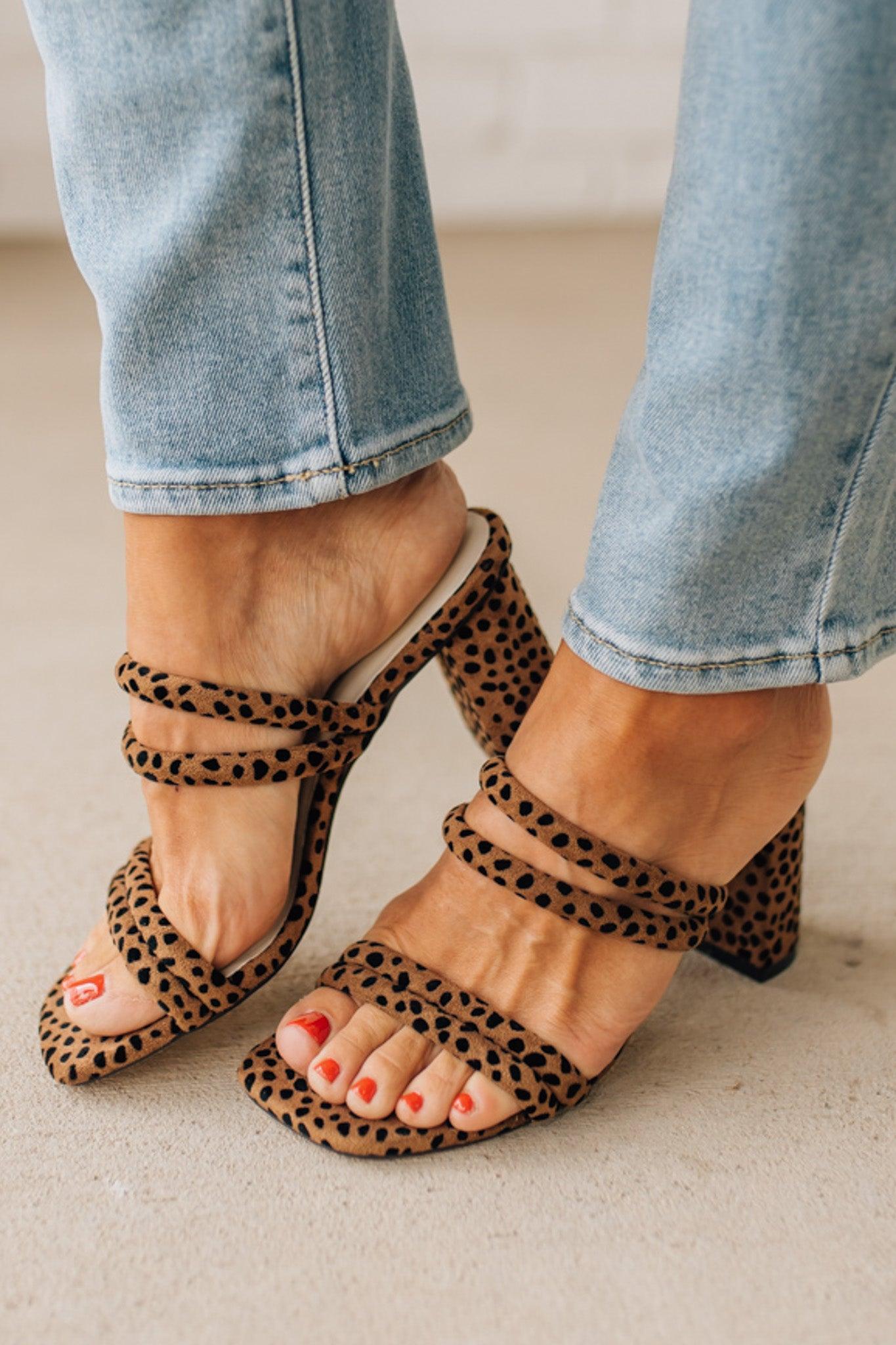 Leopard print sandals worn with light blue jeans on a neutral background