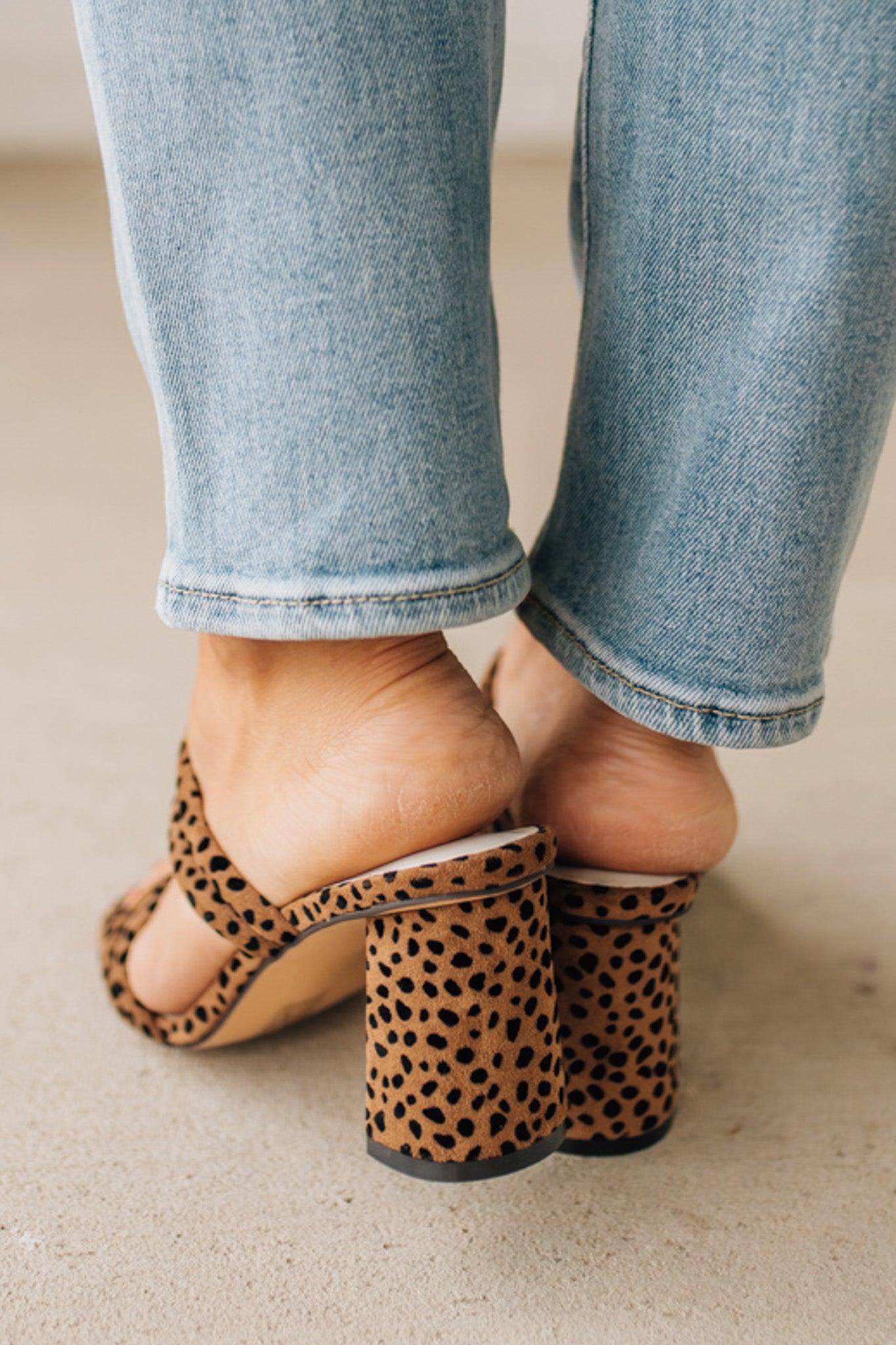 Close-up of leopard print sandals worn with light blue jeans on a neutral background