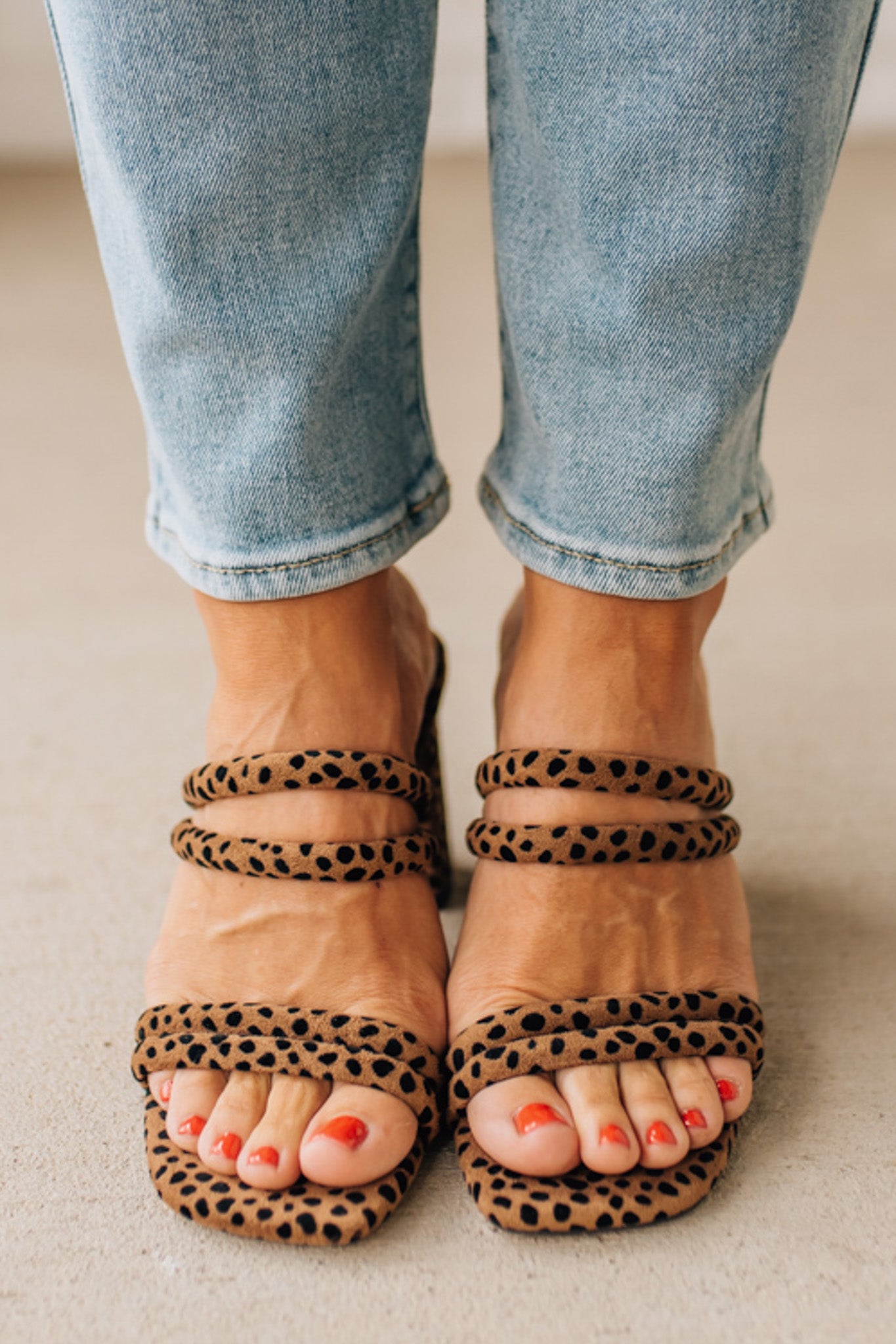 Person wearing leopard print sandals with rolled-up jeans on a neutral background