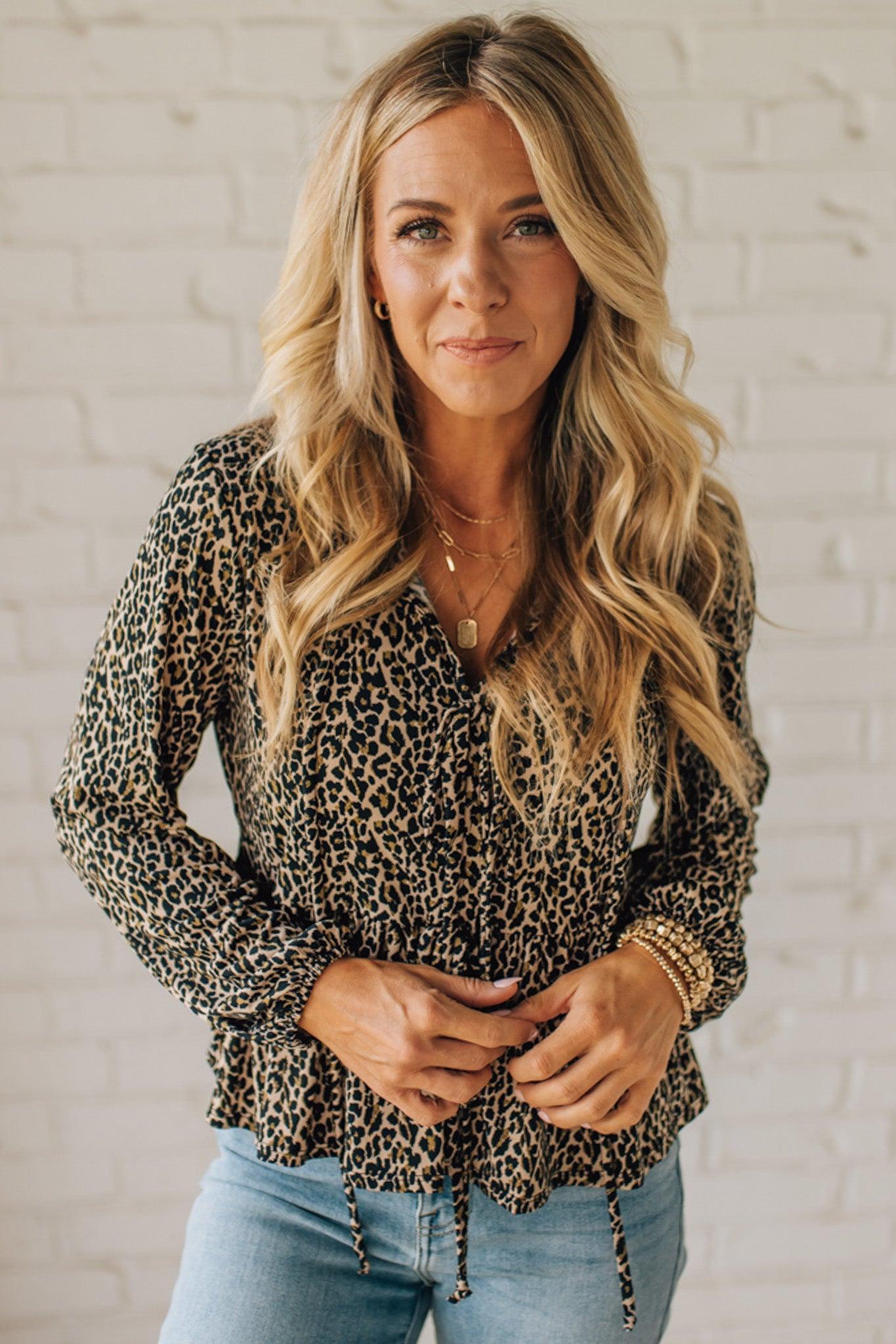 Woman wearing a leopard print top and blue jeans against a white brick wall.