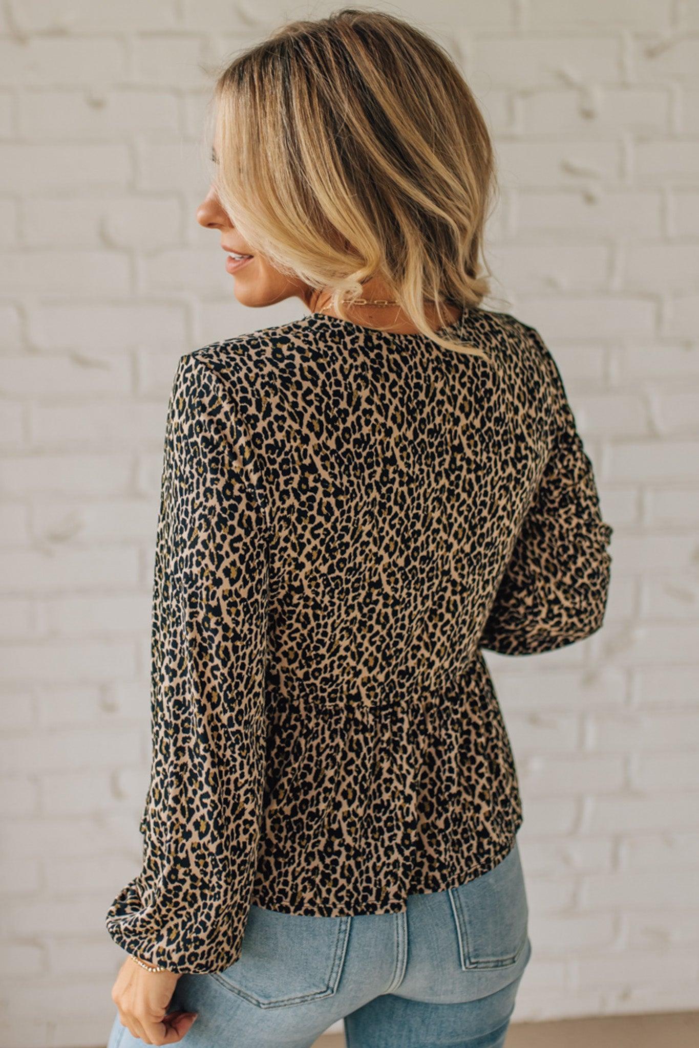 Woman wearing a leopard print long-sleeve top and jeans against a white brick wall.