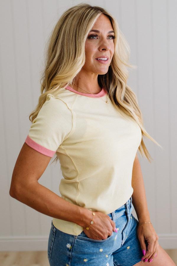 Woman wearing a yellow top with pink trim and blue jeans against a neutral background