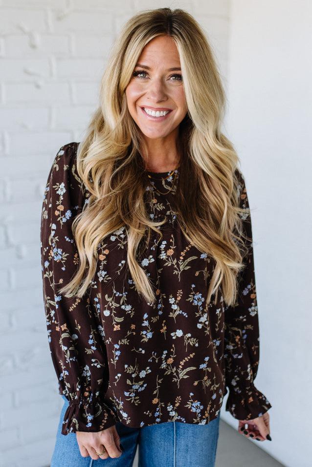 Woman wearing a floral blouse against a white brick wall