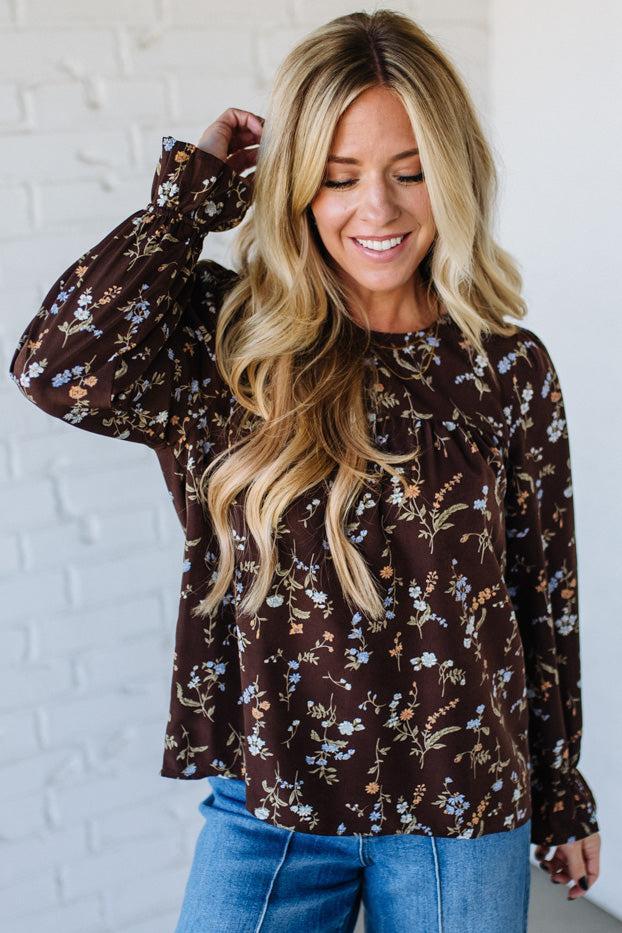 Woman wearing a brown floral blouse against a white brick wall
