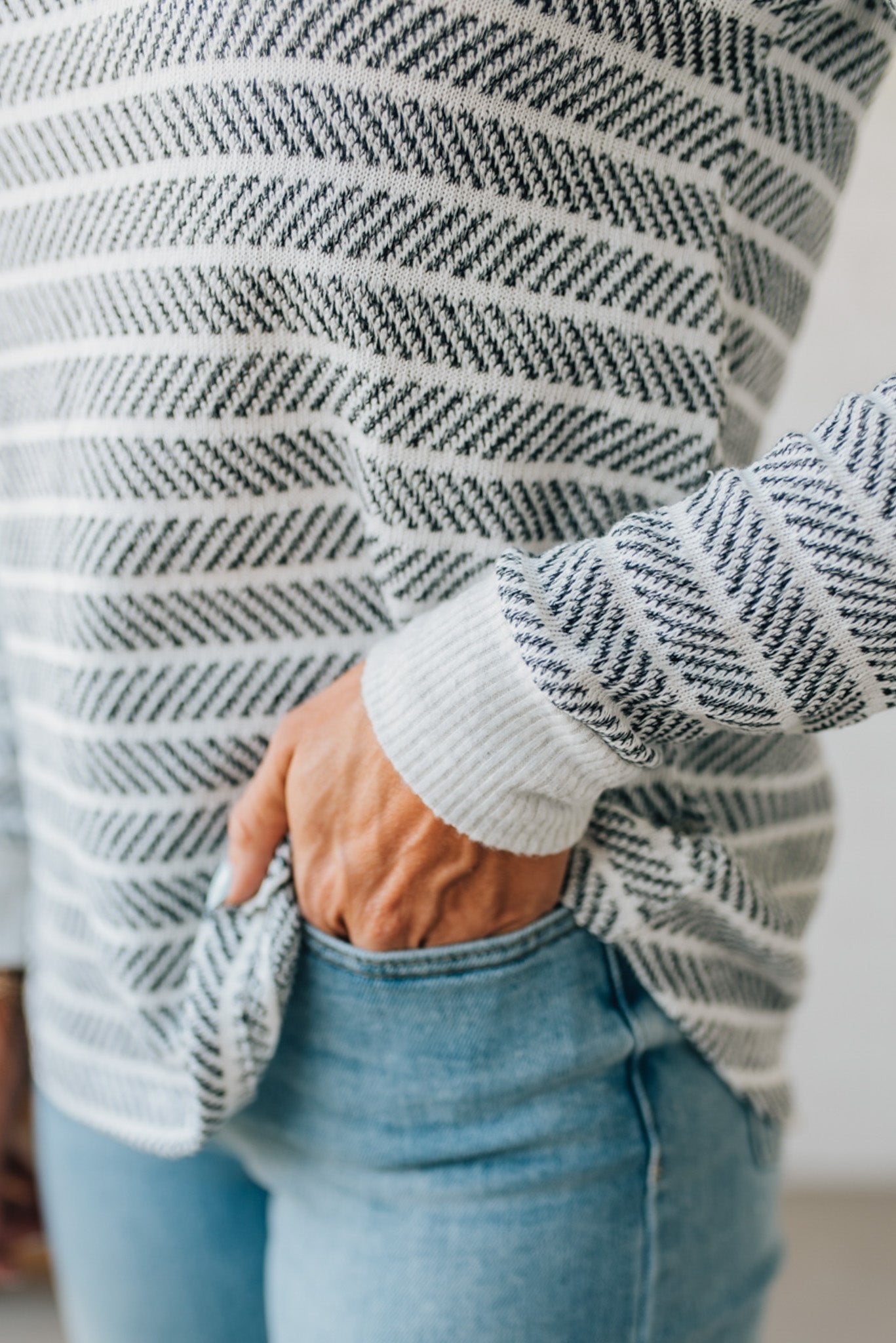 Person wearing a striped sweater and jeans with a blurred background
