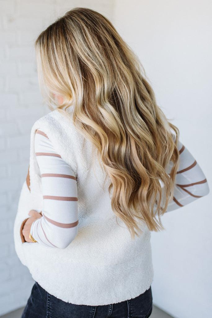 Person wearing a white sweater with sheer sleeves against a plain background