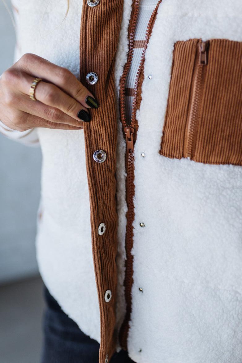 Close-up of a person wearing a white sweater with brown corduroy accents and buttons.
