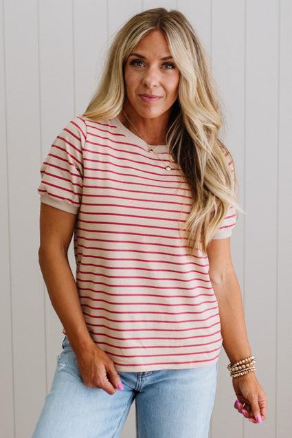 Woman wearing a red and white striped shirt with light blue jeans against a white wall.
