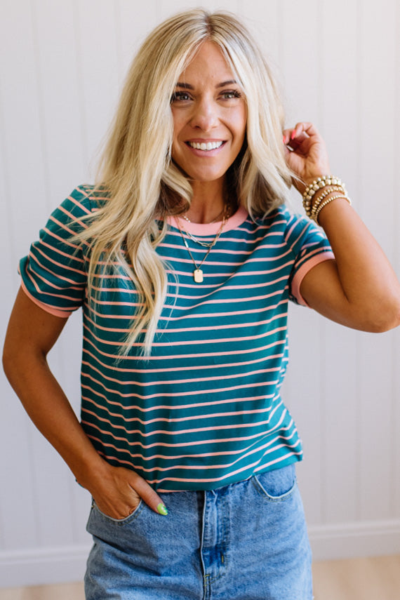 Woman wearing a striped shirt and jeans, smiling and posing with one hand on her hair.