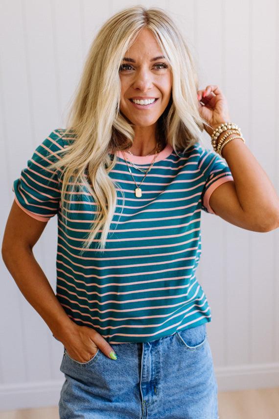 Woman wearing a striped shirt and jeans, smiling and posing with one hand on her hair.
