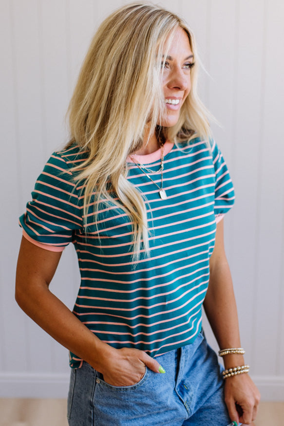 Woman wearing a green and white striped shirt with denim shorts, standing against a plain background.