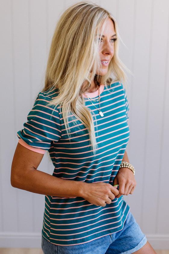 Woman wearing a blue and green striped shirt with denim shorts against a plain background