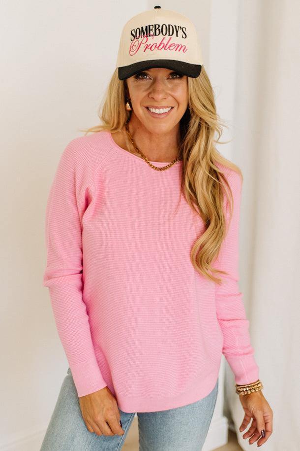 Blonde woman wearing jeans and a pink sweater with a black and white hat and sneakers.