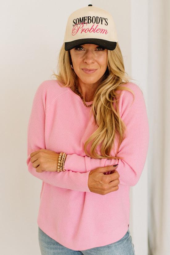 Blonde woman wearing jeans and a pink sweater with a black and white hat and sneakers.
