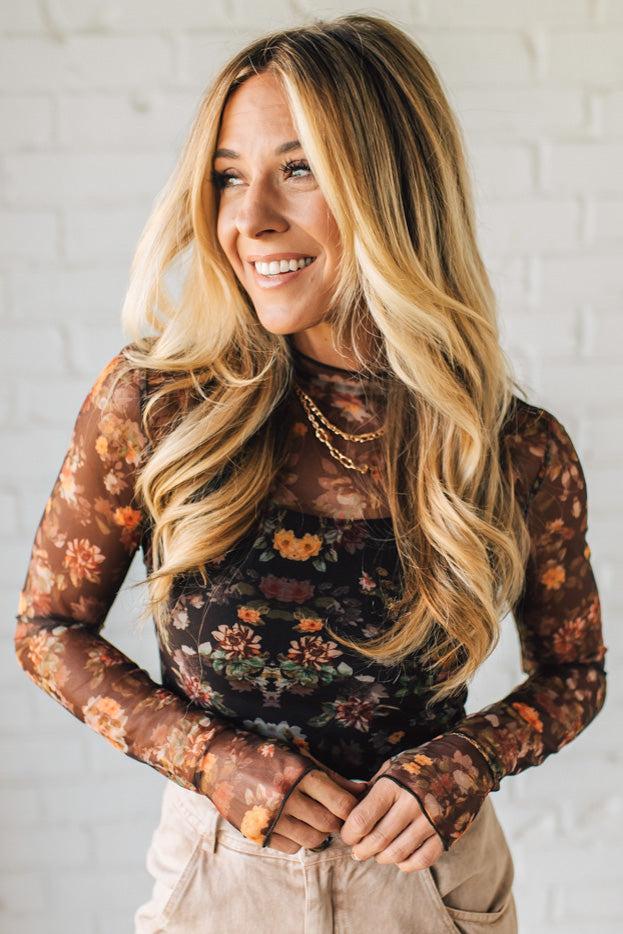 Woman wearing a floral long-sleeve top against a white brick wall