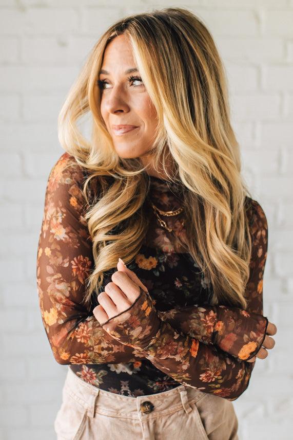 Woman wearing a floral blouse against a white brick wall