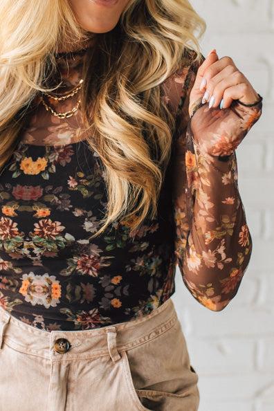 Person wearing a floral long-sleeve top and beige pants against a white background