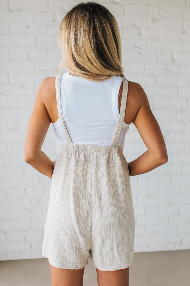 Blonde woman wearing a gauze textured short romper with adjustable knot straps.