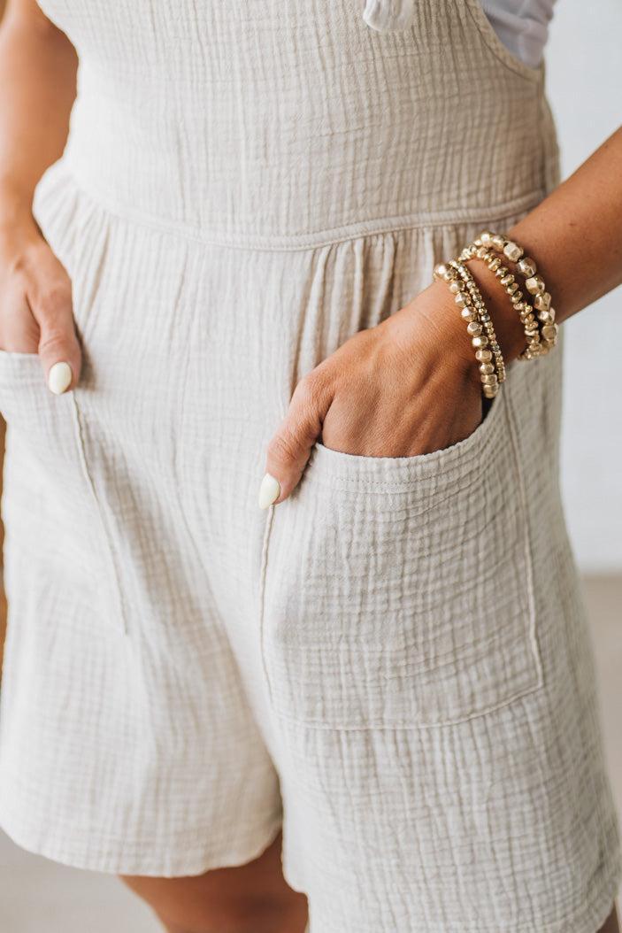 Blonde woman wearing a gauze textured short romper with adjustable knot straps.