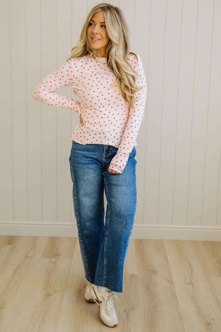 Woman wearing a polka dot blouse and jeans standing against a white paneled wall.