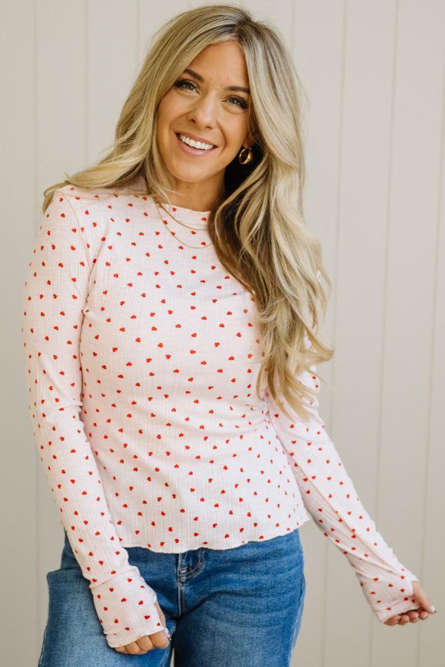 Woman wearing a white long-sleeve top with red patterns and blue jeans against a light background