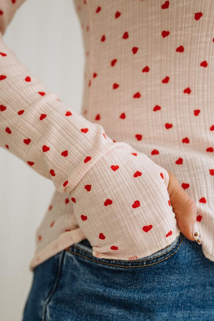 Person wearing a beige top with red heart patterns and blue jeans.