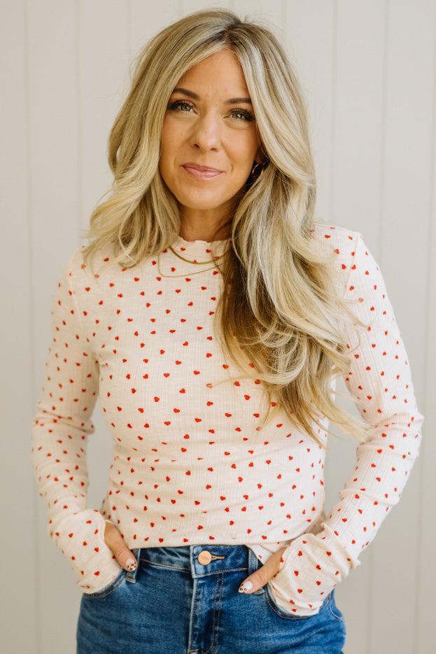 Woman wearing a white long-sleeve top with red polka dots and blue jeans against a neutral background