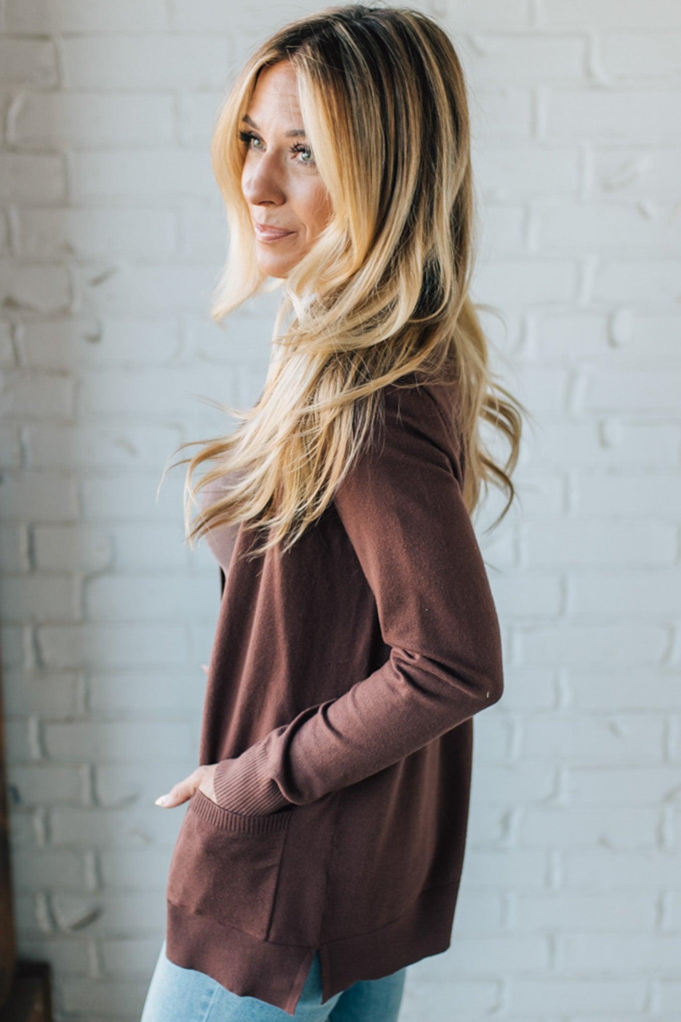 Woman wearing a brown sweater against a white brick wall