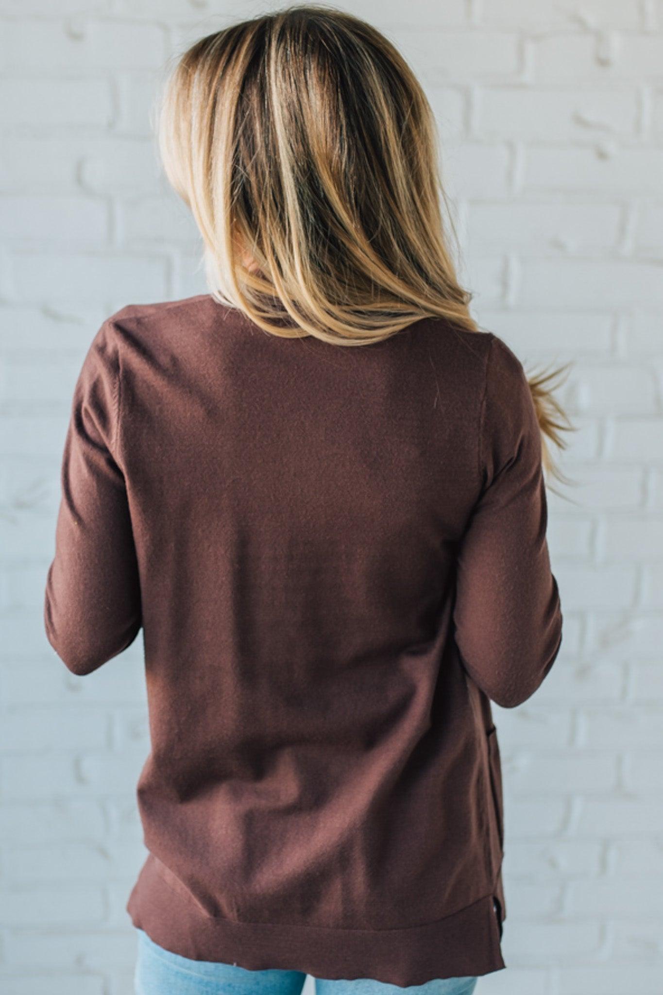 Person wearing a brown sweater with a white brick wall background