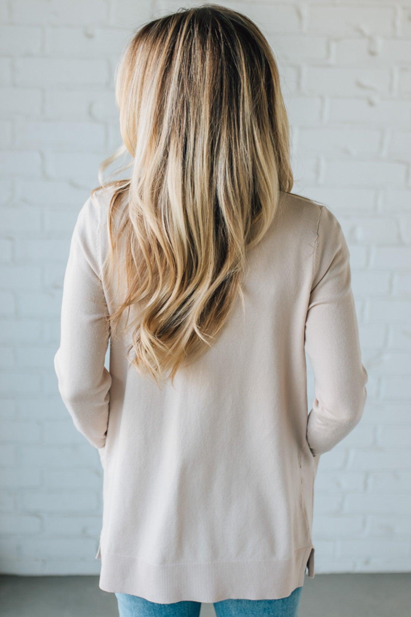 Person wearing a beige cardigan against a white brick wall