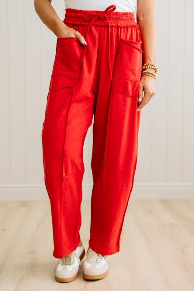 Person wearing red pants with pockets on a light wooden floor.