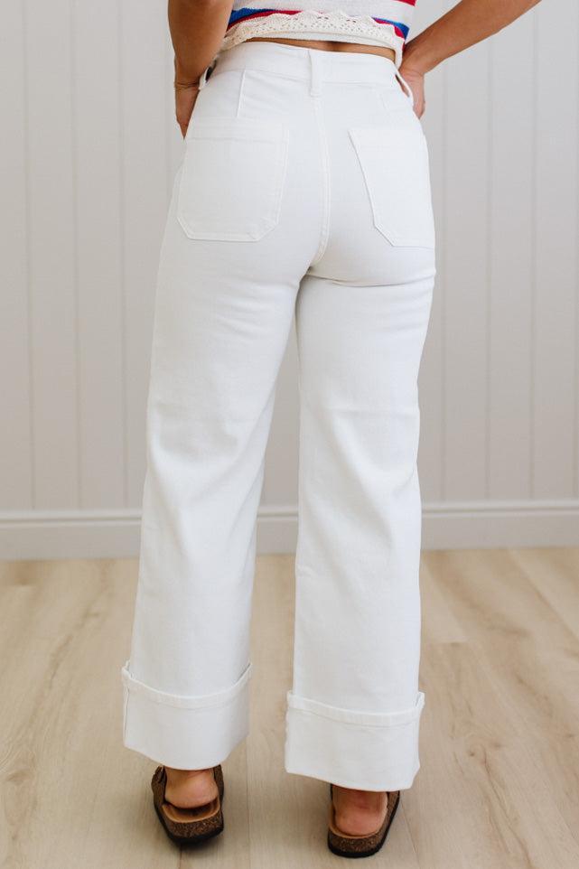 White pants worn by a person on a light wooden floor with a white wall background