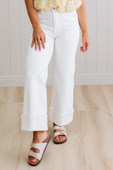 Person wearing white pants and a colorful top on a light wooden floor.