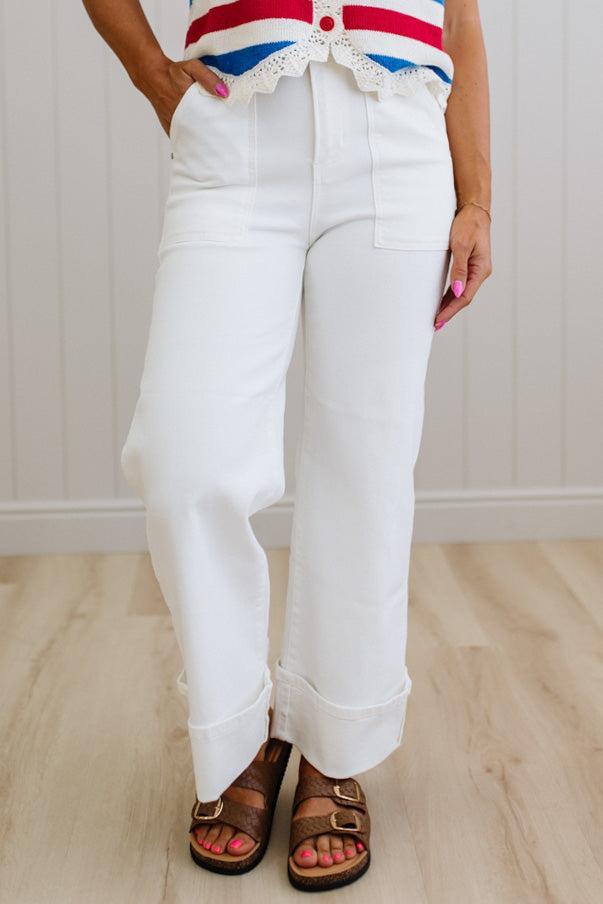 Person wearing white pants and a colorful top on a light wooden floor.