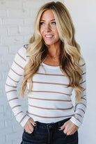 Woman wearing a white and brown striped long-sleeve top against a white brick wall.