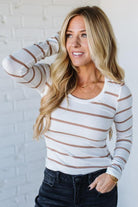 Woman wearing a striped long-sleeve top against a white brick wall