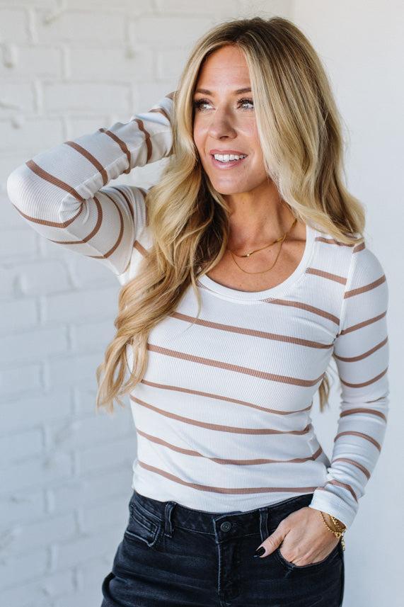 Woman wearing a striped long-sleeve top against a white brick wall