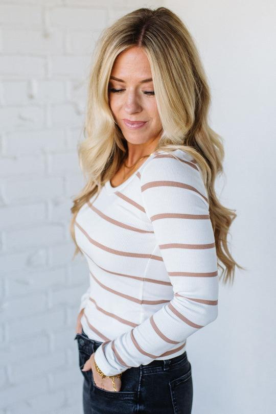 Woman wearing a white and brown striped long-sleeve top against a light gray background