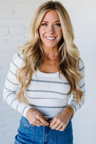 Woman wearing a striped long-sleeve top and blue jeans against a white background