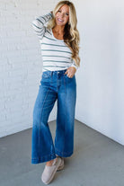 Woman wearing a striped shirt and blue jeans against a white brick wall.