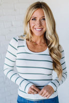 Woman wearing a striped long-sleeve top against a white brick wall.