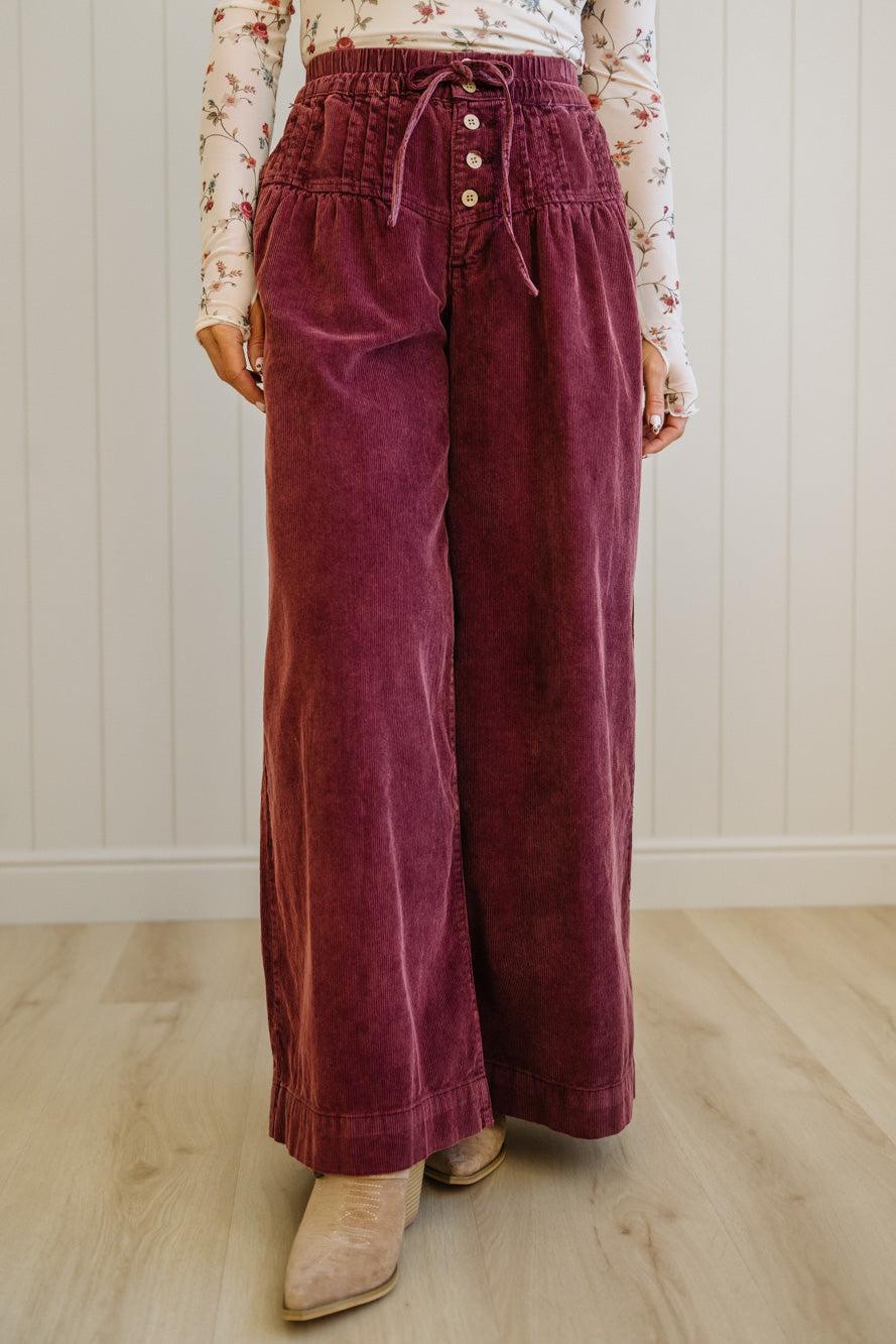 Maroon corduroy pants worn by a person on a light wooden floor.