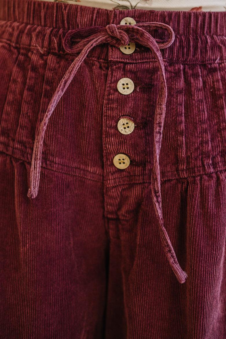 Close-up of maroon corduroy pants with button details and a drawstring.