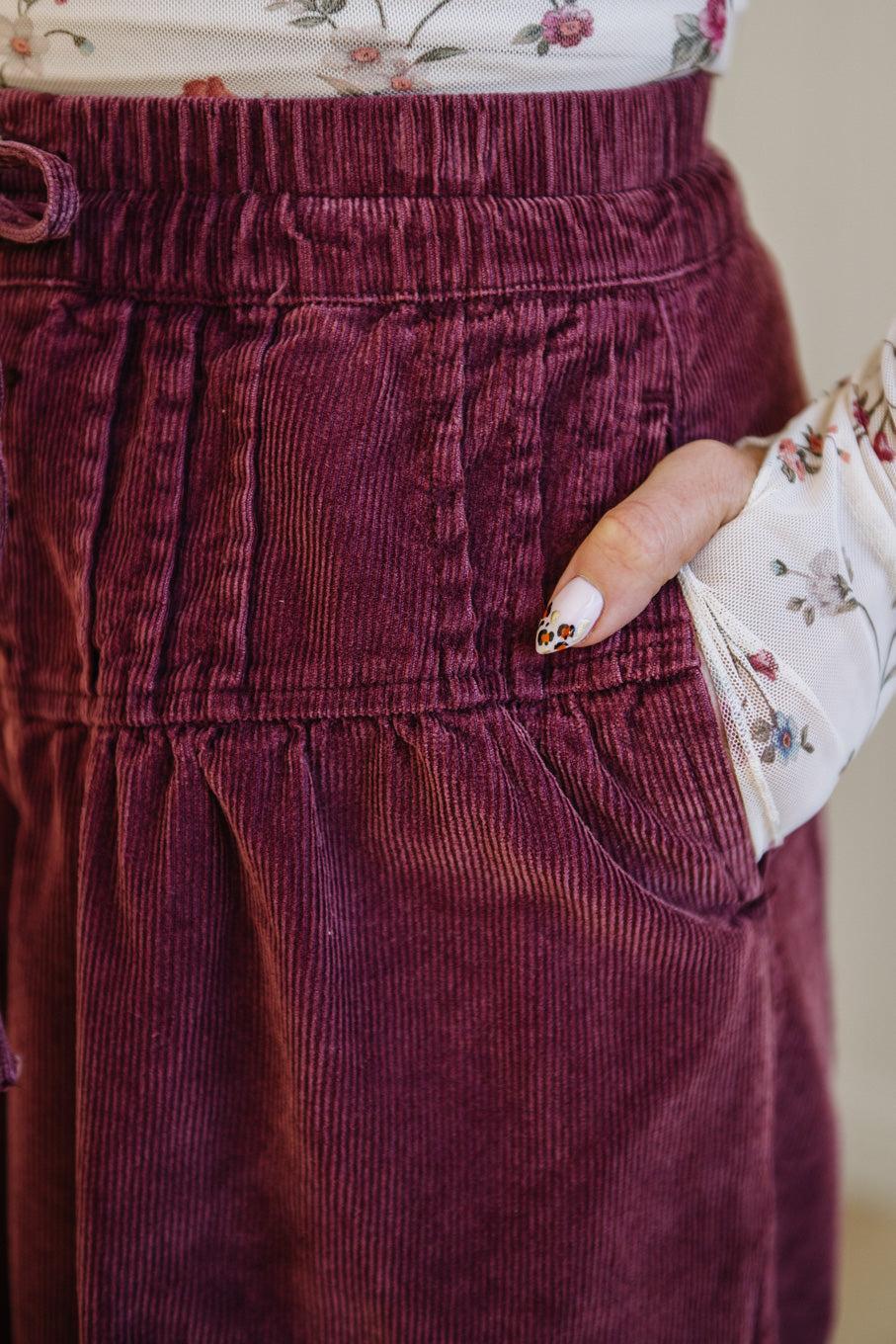 Close-up of maroon corduroy pants with a floral top underneath.
