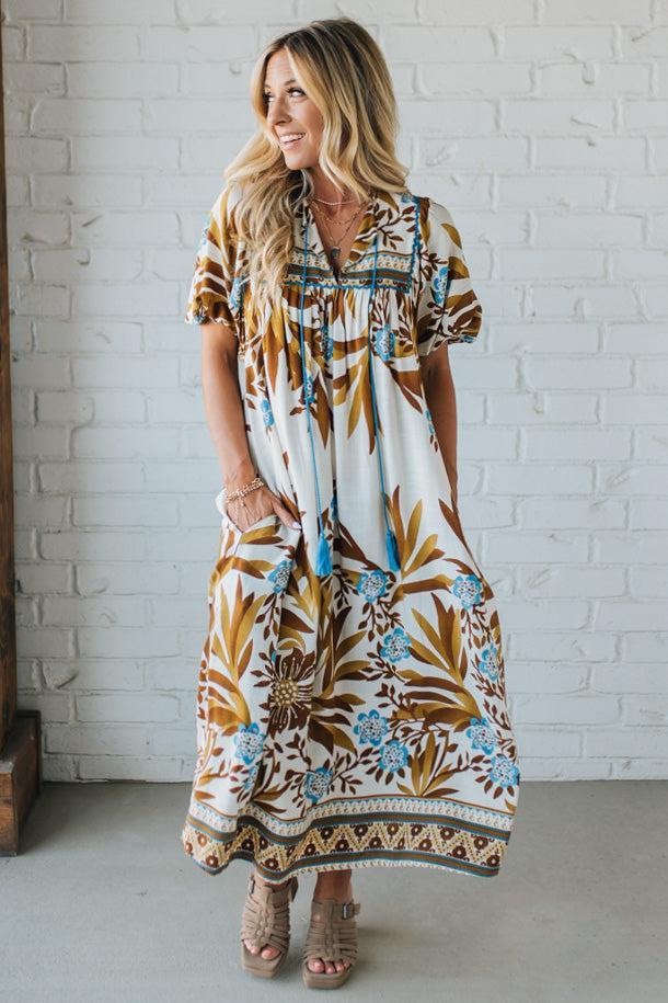 Woman wearing a patterned dress standing against a white brick wall.