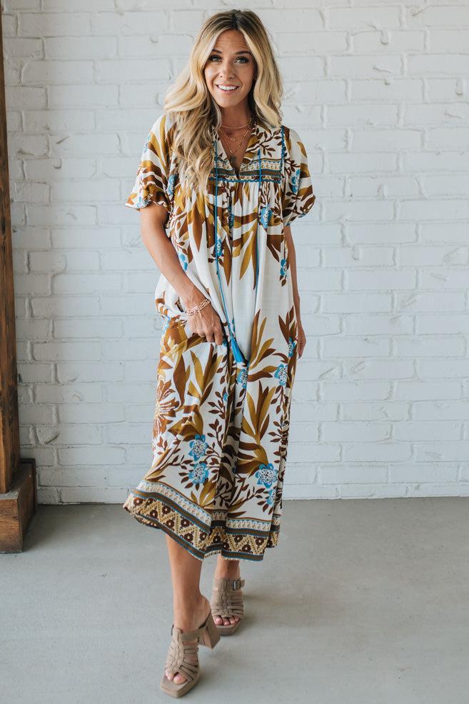 Woman wearing a patterned dress standing against a white brick wall.