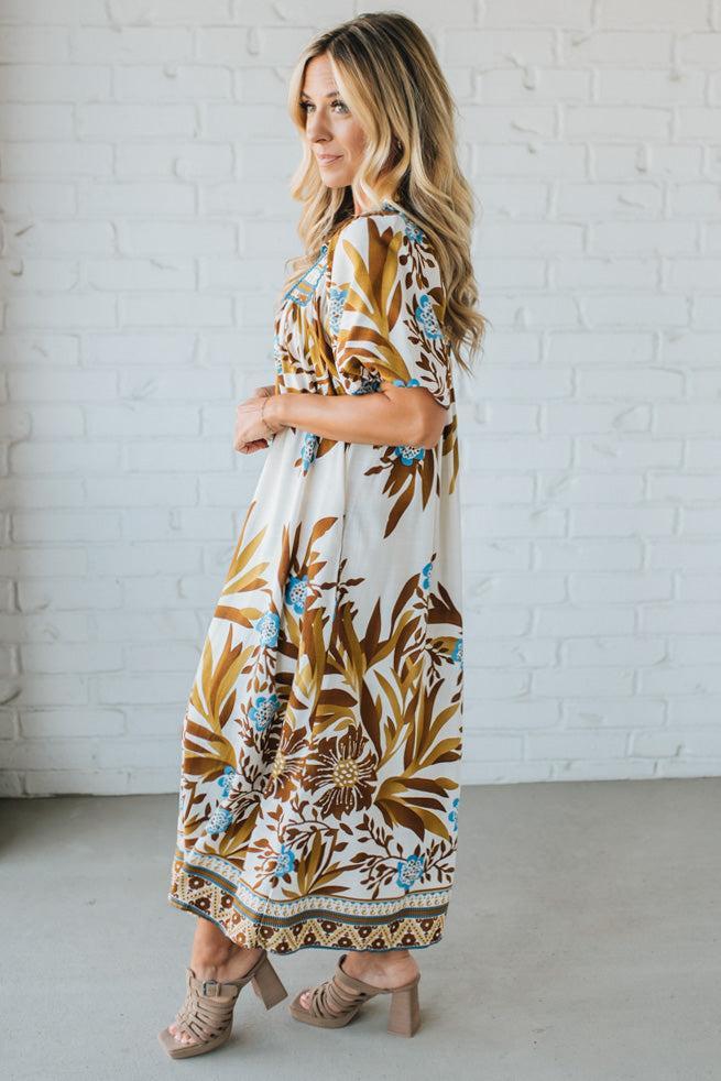 Woman wearing a floral dress against a white brick wall.