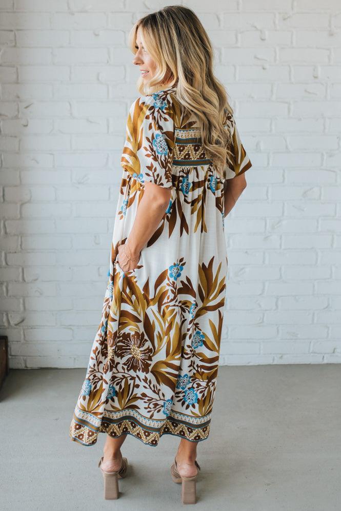 Woman wearing a patterned dress standing against a white brick wall.